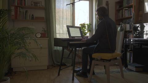 A musician seated at a piano, bathed in natural light, surrounded by books and art.