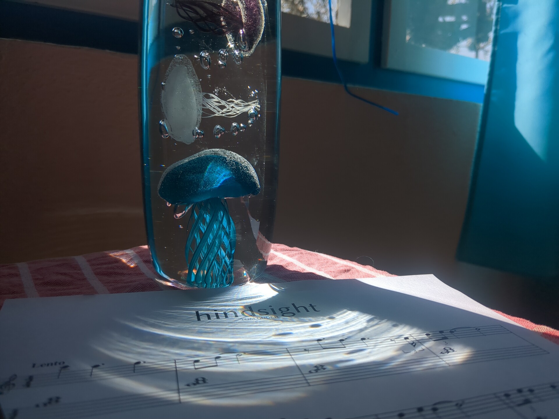 A glass vial containing preserved life rests beside sheet music illuminated by natural light.