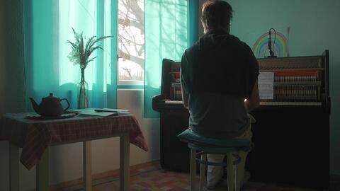 A figure seated at a piano bathed in soft, creative window light.