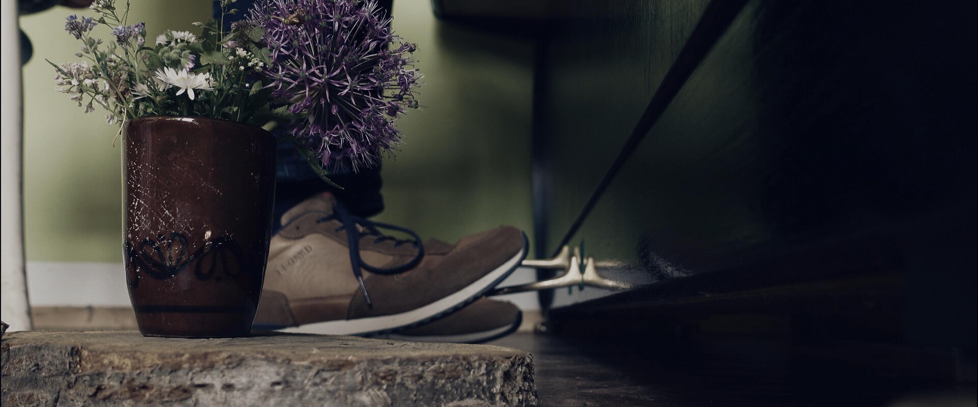 Fresh flowers and worn shoes resting beside a dark, elegant piano.